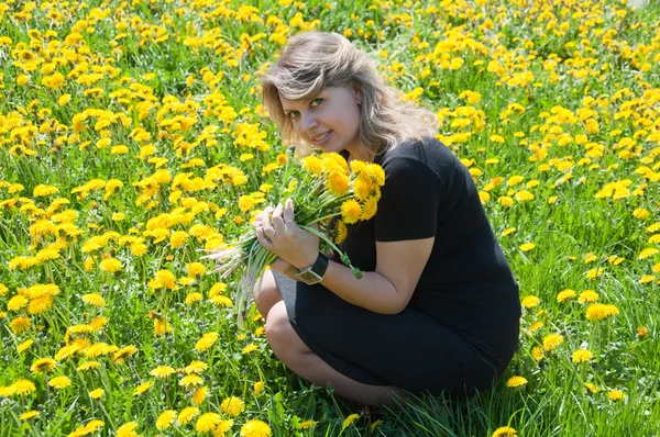 Retrato de uma jovem no gramado com um buquê de dentes-de-leão — Fotografia de Stock