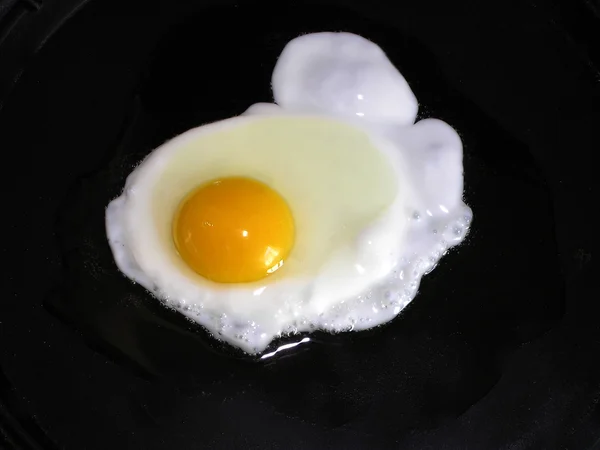 Un uovo viene cucinato in una padella  . Fotografia Stock