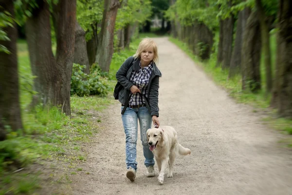 Blonde vrouw wandelen met haar gouden retriever hond in het park — Stockfoto