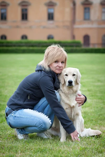 金髪の女性が公園で彼女のゴールデン ・ リトリーバー犬を連れて歩いて — ストック写真
