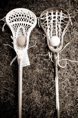 Two lacrosse heads and sticks with ball on grass - black and whi clipart