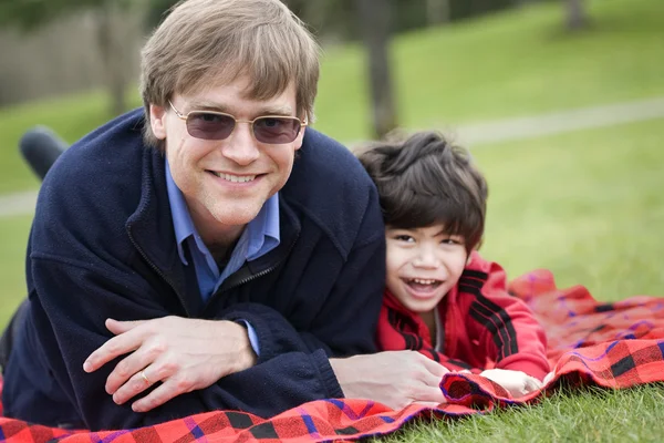 Padre acostado en manta con hijo discapacitado en el parque —  Fotos de Stock