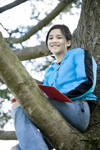 Девочка-подросток, сидящая на дереве, пишет в дневнике или блокноте — стоковое фото
