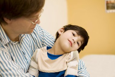 Father holding disabled son in doctor's office clipart