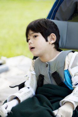 Four year old boy disabled with cerebral palsy sitting outdoors clipart