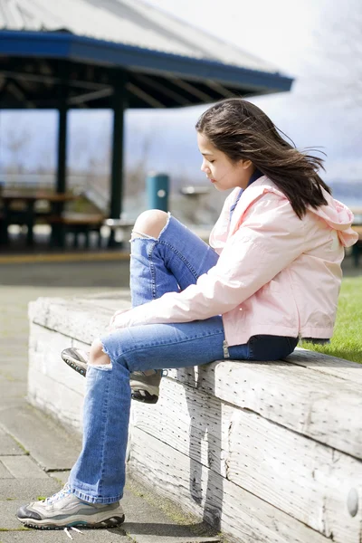 Preteen girl tying shoes outdoors near lake — Stock Photo, Image
