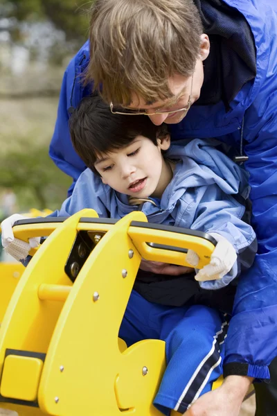 Pai ajudando filho deficiente jogar em equipamentos de playground — Fotografia de Stock