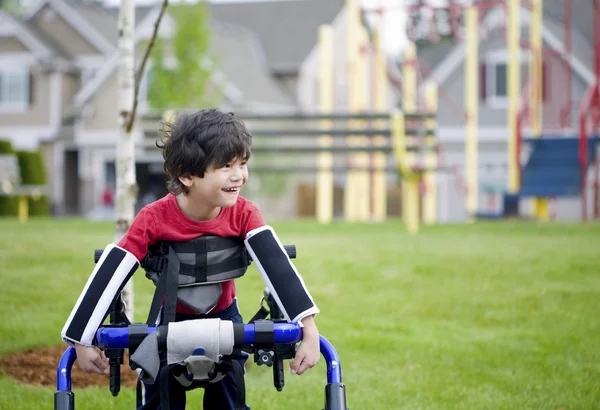 Deficiente menino de quatro anos de pé em walker perto de um parque infantil — Fotografia de Stock
