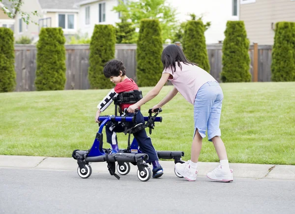 Grande sœur aidant jeune frère handicapé dans walker — Photo