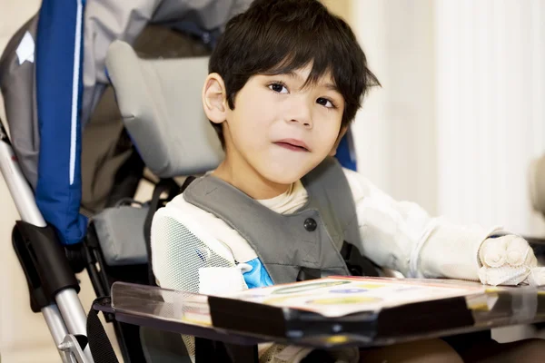 Niepełnosprawnych 4-letniego chłopca badanie albo czytanie na wózku inwalidzkim — Zdjęcie stockowe