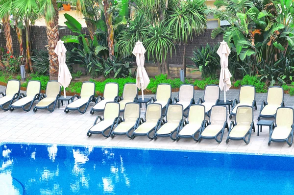 Plastikstühle und Sonnenschirme in der Nähe des Schwimmbades — Stockfoto