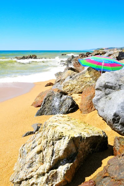 Empty beach with rocks and sun umbrella — Stock Photo, Image