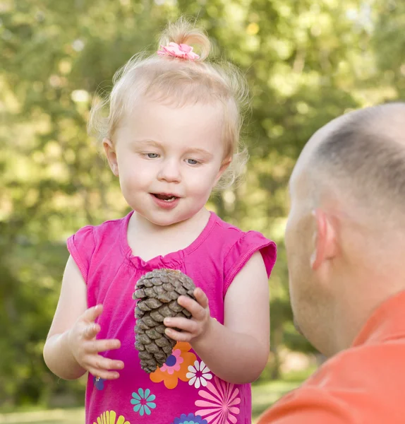 Молодая девушка держит сосновую шишку со своим отцом в парке — стоковое фото