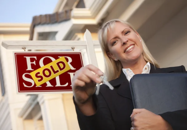 Agente inmobiliario con llaves en frente del letrero vendido y la casa —  Fotos de Stock