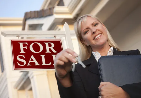 Agente inmobiliario con llaves en frente del cartel y la casa —  Fotos de Stock