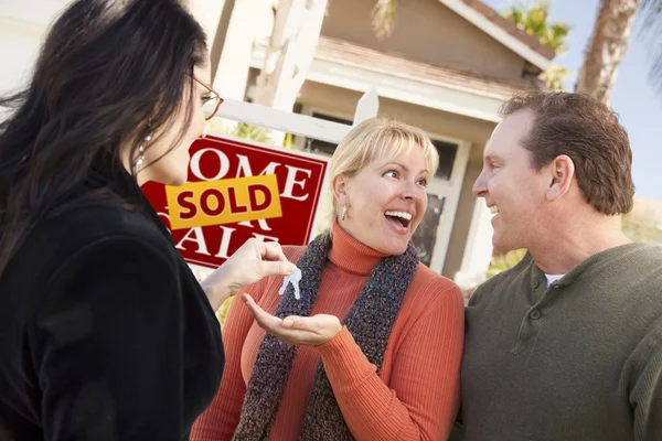 Hispânico feminino agente imobiliário entregando chaves para casal excitado — Fotografia de Stock