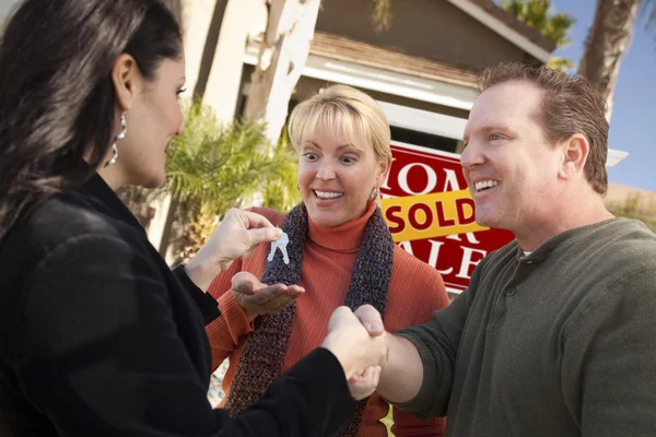 Hispânico feminino agente imobiliário entregando chaves para casal excitado — Fotografia de Stock