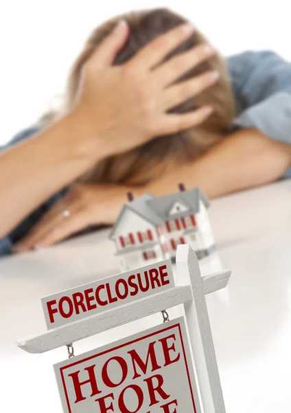 Mujer, la cabeza en la mano detrás de la casa modelo y el signo de ejecución hipotecaria —  Fotos de Stock