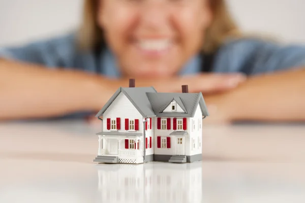 Mulher sorridente por trás da casa modelo em uma superfície branca — Fotografia de Stock