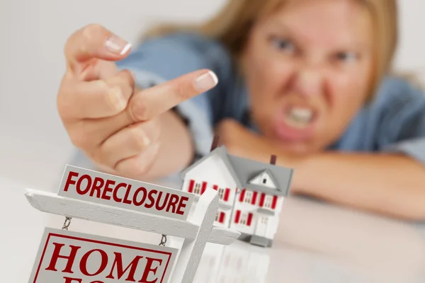 Mujer volteando el pájaro detrás de la casa modelo y el signo de ejecución hipotecaria — Foto de Stock