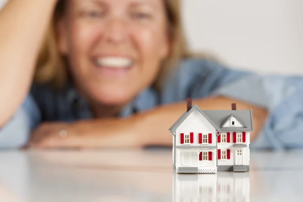 Mujer sonriente detrás de la casa modelo en una superficie blanca — Foto de Stock