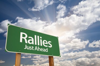 Rallies Green Road Sign Against Clouds clipart