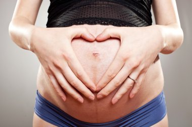 Woman making a heart with hands on her belly clipart