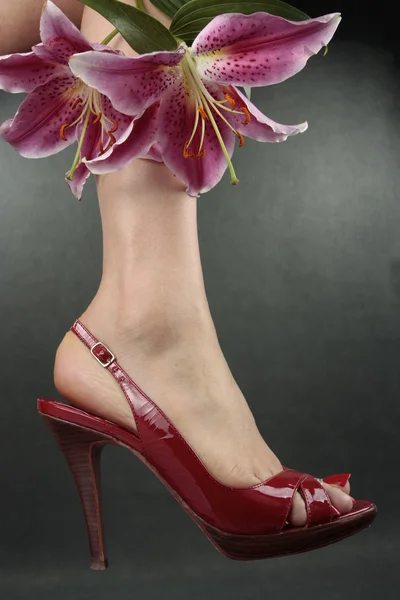 Kvinna ben bära höga klackar med blommor över grå bakgrund — Stockfoto