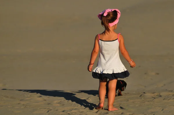 Egy gyönyörű kis lány játszani, és ugrik a kutya a strandon — Stock Fotó