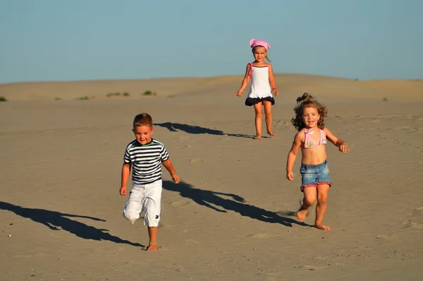 Duas meninas e um menino brincando na areia da praia — Fotografia de Stock