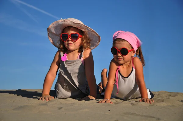 Twee kleine meisjes liggend op het zandstrand — Stockfoto