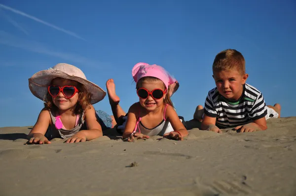 Dos niñas y un niño tumbados en la playa de arena —  Fotos de Stock