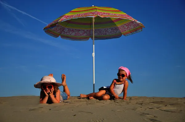 Two little girls on the beach under a beach umbrella — Stock Photo, Image