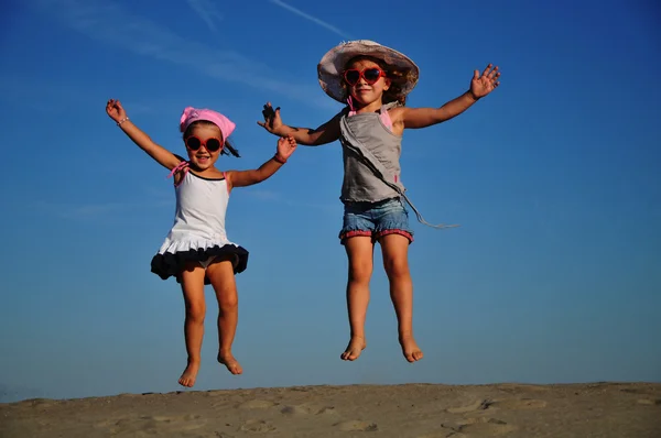Dvě šťastná holčička skákání na pláži — Stock fotografie