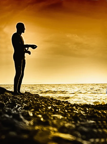 年轻男子站在湿沙在明亮的日落背景 — 图库照片