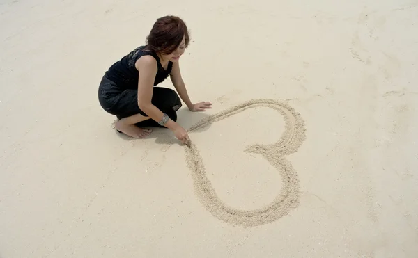 Fotografia di una bella donna disegnare la forma dell'amore sulla spiaggia durante le vacanze Immagine Stock