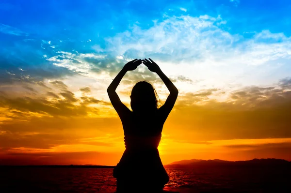 Silhouette di donna si esibisce come esercizio di yoga sulla spiaggia durante il tramonto Foto Stock