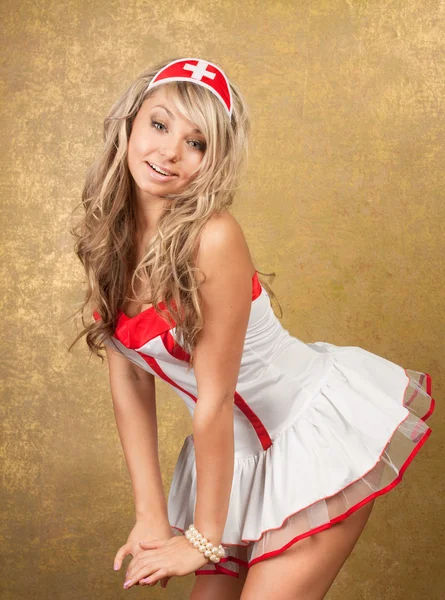 Sexy blondýnka svůdná zdravotní sestra kostým na zlaté poza — Stock fotografie