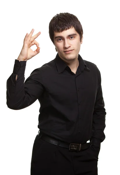 Portrait of young man in black shirt gesturing ok sign against w — Stock Photo, Image