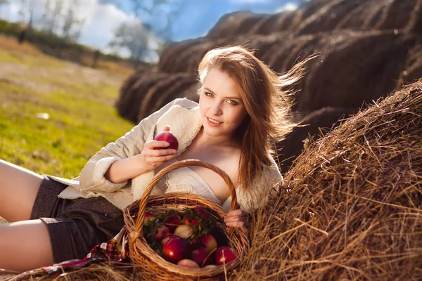Wunderschöne lächelnde Frau mit vielen Apfel im Korb auf Heuhaufen am — Stockfoto