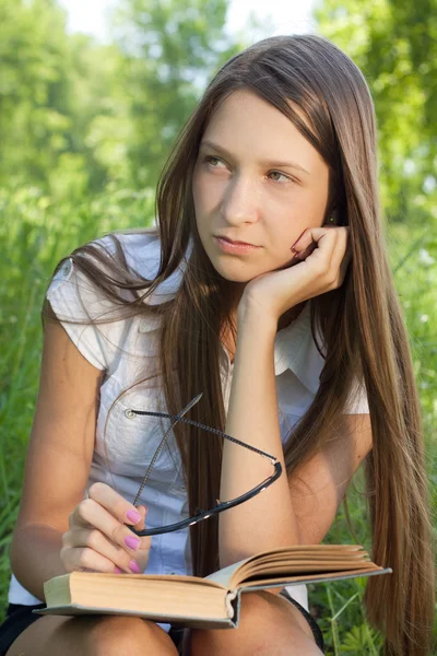 Young student girl sitting in park with book lizenzfreie Stockfotos