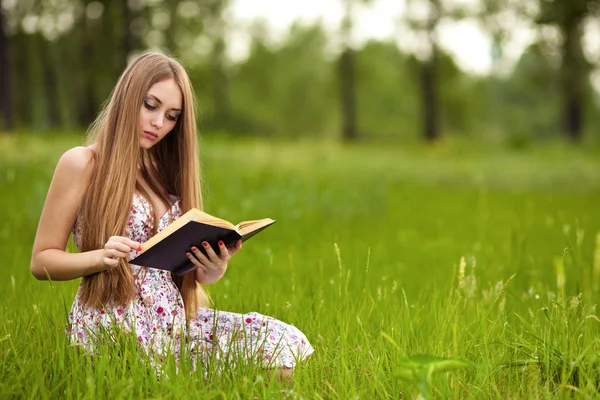 Menina-estudante sentar-se no gramado e lê livro didático . — Fotografia de Stock