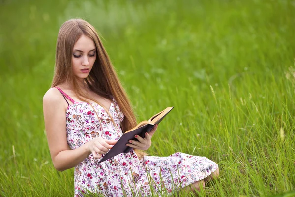 Chica-estudiante sentarse en el césped y lee libro de texto . —  Fotos de Stock