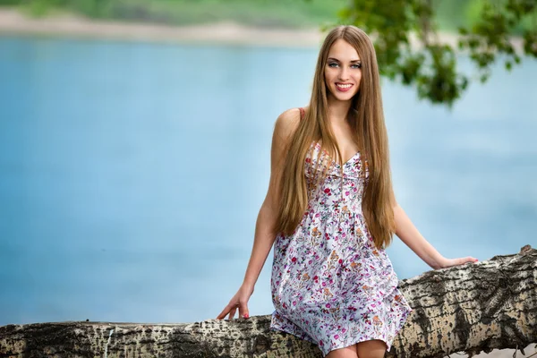 Jonge vrouw zitten op log in het park in de buurt van de rivier — Stockfoto
