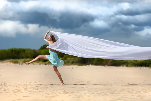 Beautiful young woman walking on the beach with a white tissue — Stok Foto
