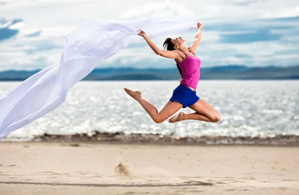Красивая молодая женщина, прыжки на пляже с белой ткани — стоковое фото