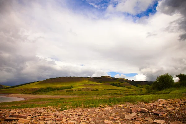 Taşlar ve bulutlu gökyüzü altında yeşil tepeler — Stok fotoğraf