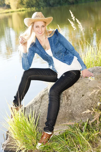 Молодая женщина, сидящая на камне у пруда — стоковое фото