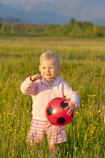 Little girl with a ball standing on meadow — Stock Photo, Image