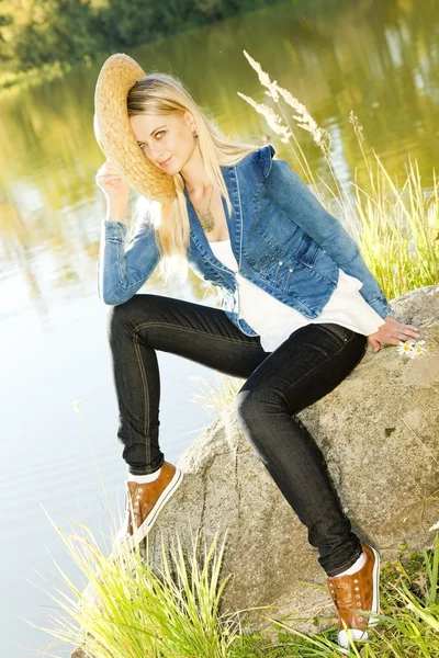 Young woman sitting on stone at pond — Stock Photo, Image